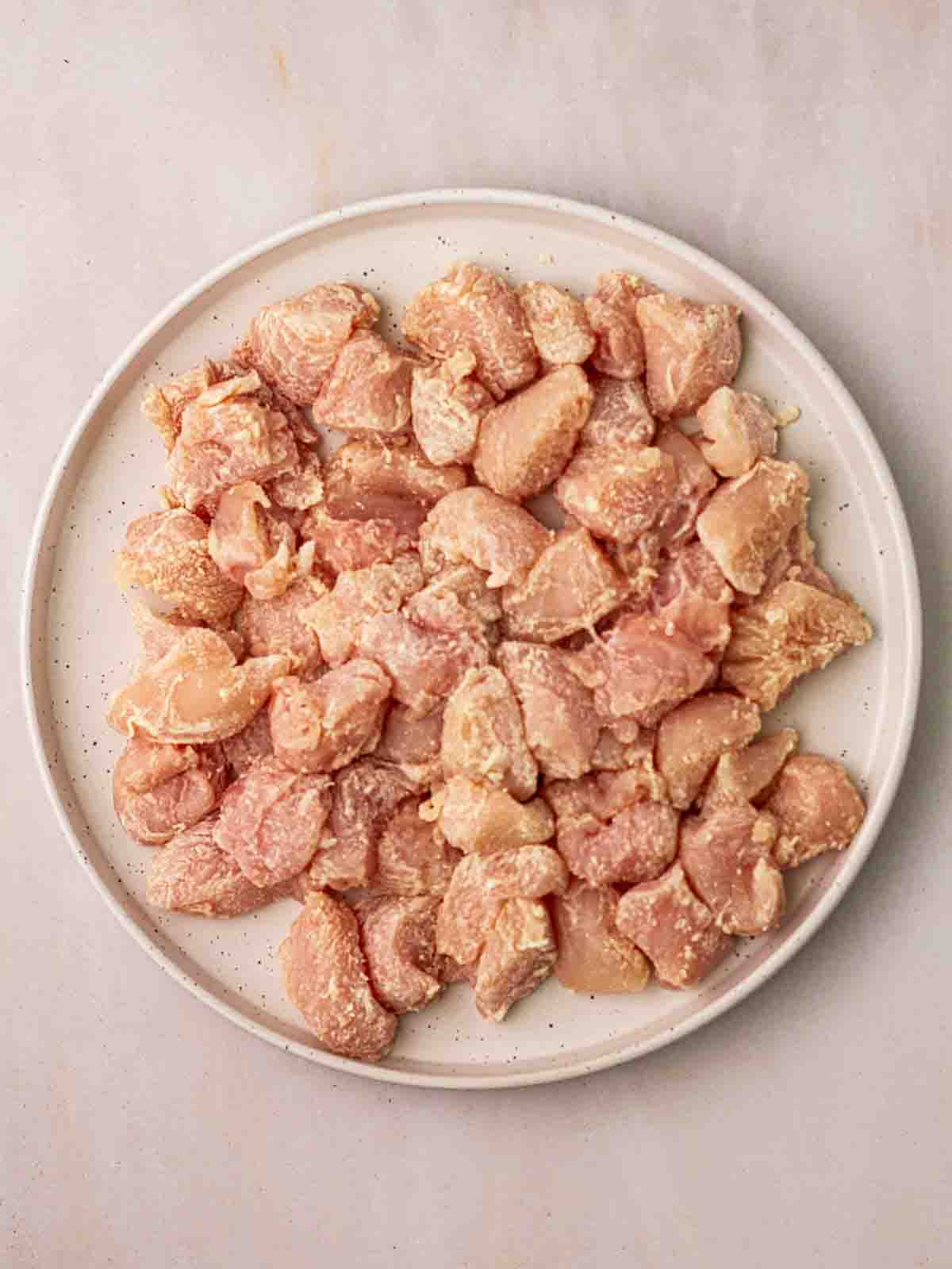 Chunks of raw chicken on a white plate, coated with flour for the recipe Slow Cooker Marry Me Chicken.