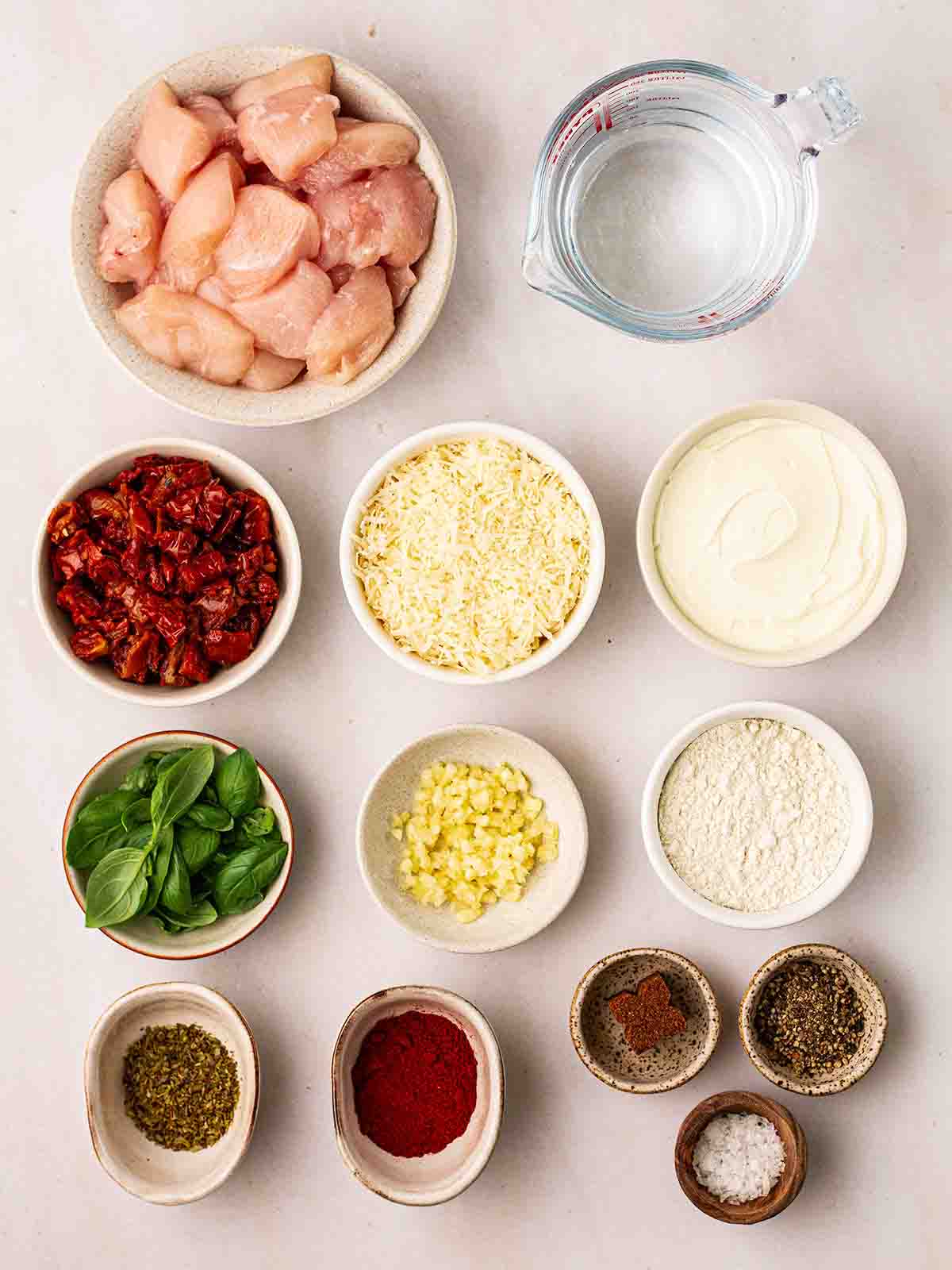 The raw ingredients for Slow Cooker Marry Me Chicken laid out in small bowls on a white counter top.