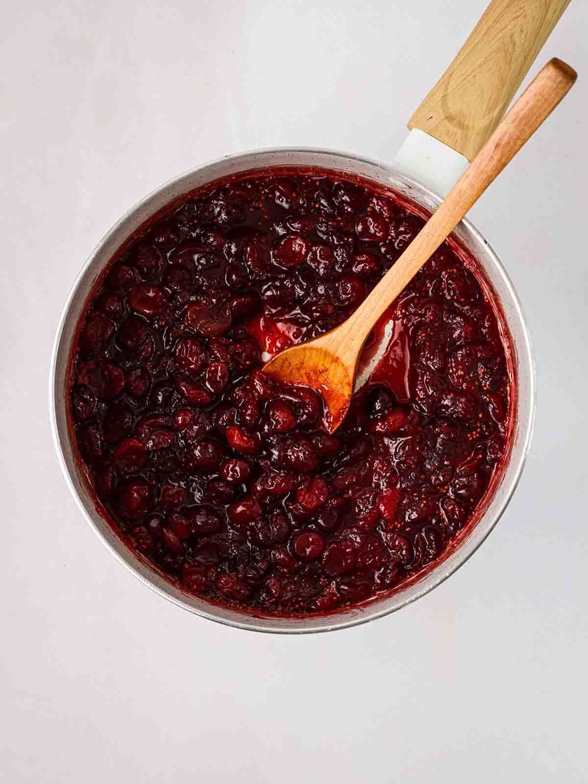 Cranberry sauce in a pan with a wooden spoon, stirring.