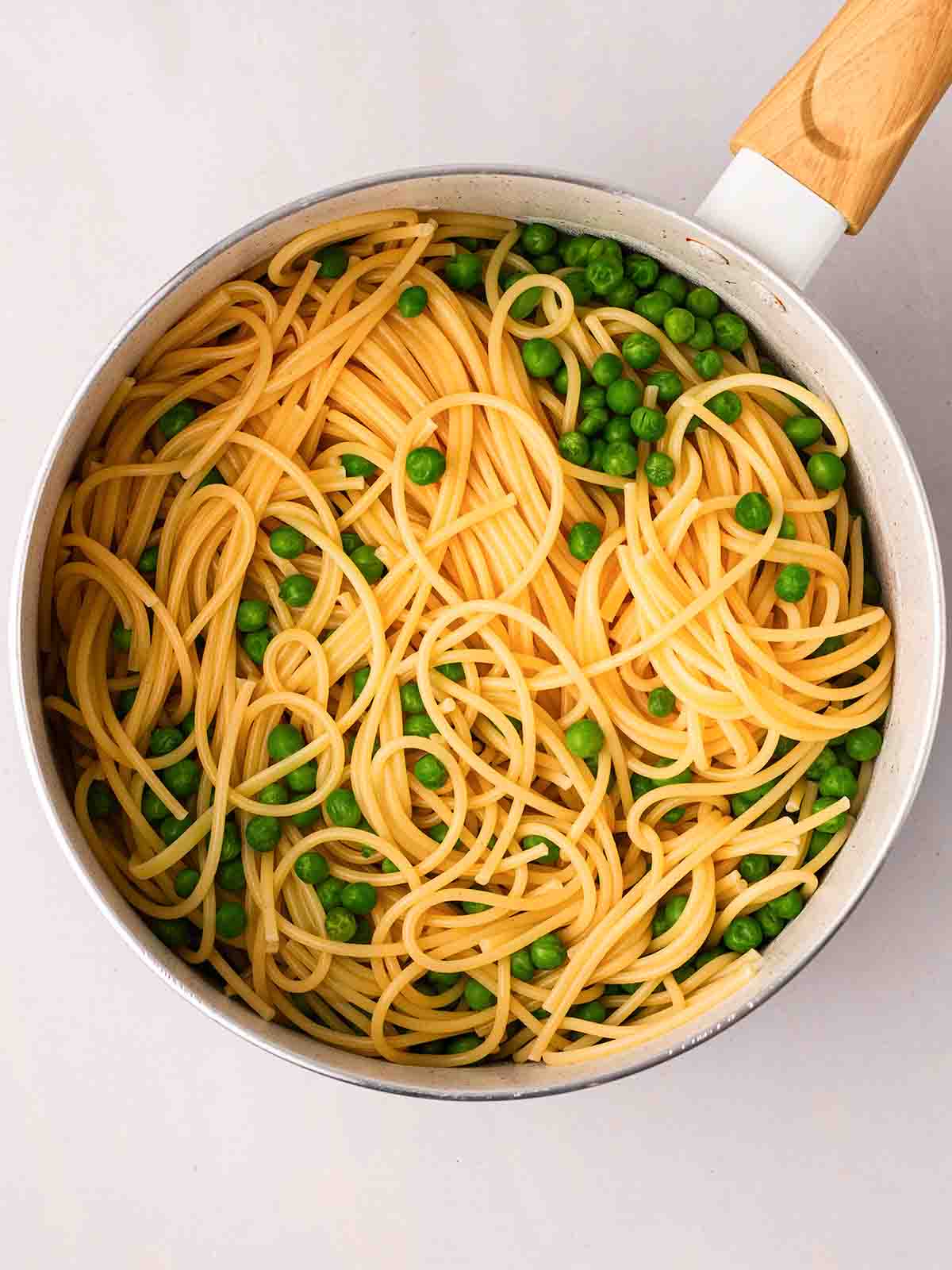 Cooked spaghetti and peas in a pan for the recipe prawn pasta.