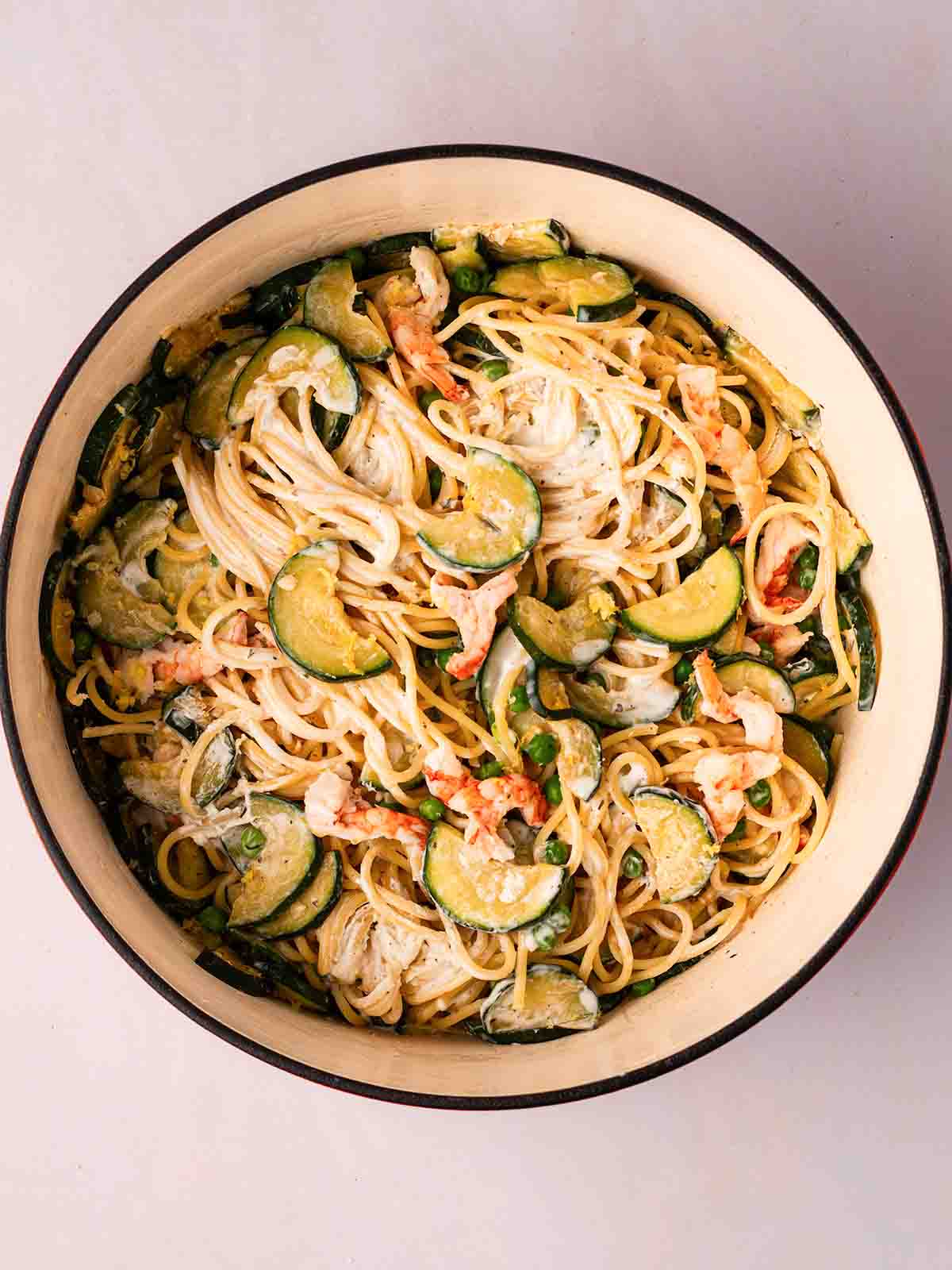 A large pan filled with creamy spaghetti sauce with courgettes and prawns.