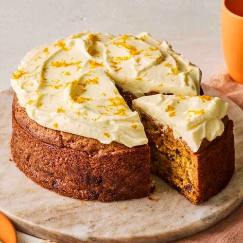 A simple carrot cake on a cake dish with a slice cut out.