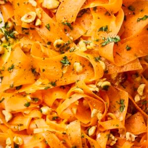 A close up of carrot ribbons in a salad with nuts and dressing.