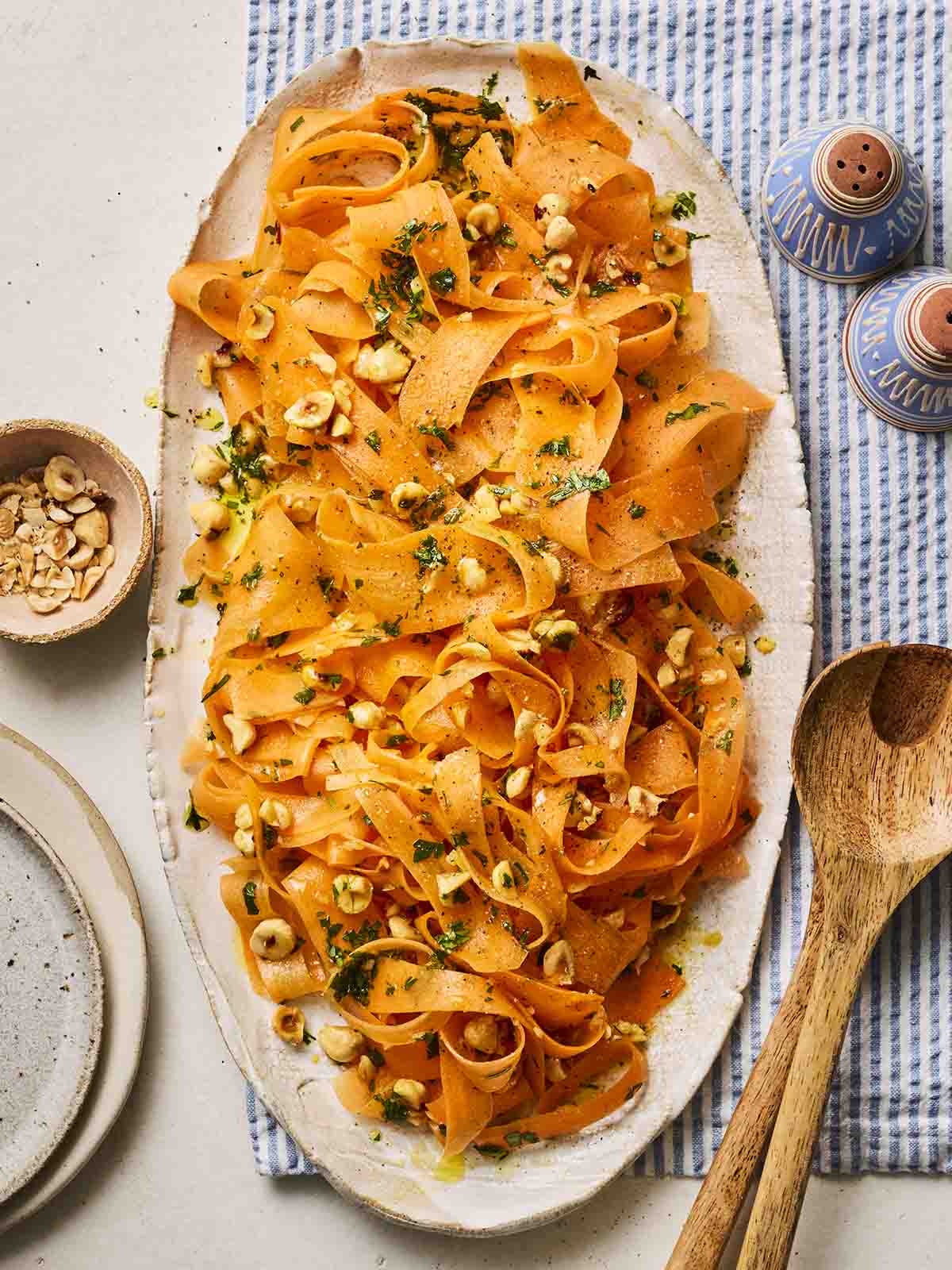 A platter of Carrot Salad, on a table ready to serve with wooden salad utensils.