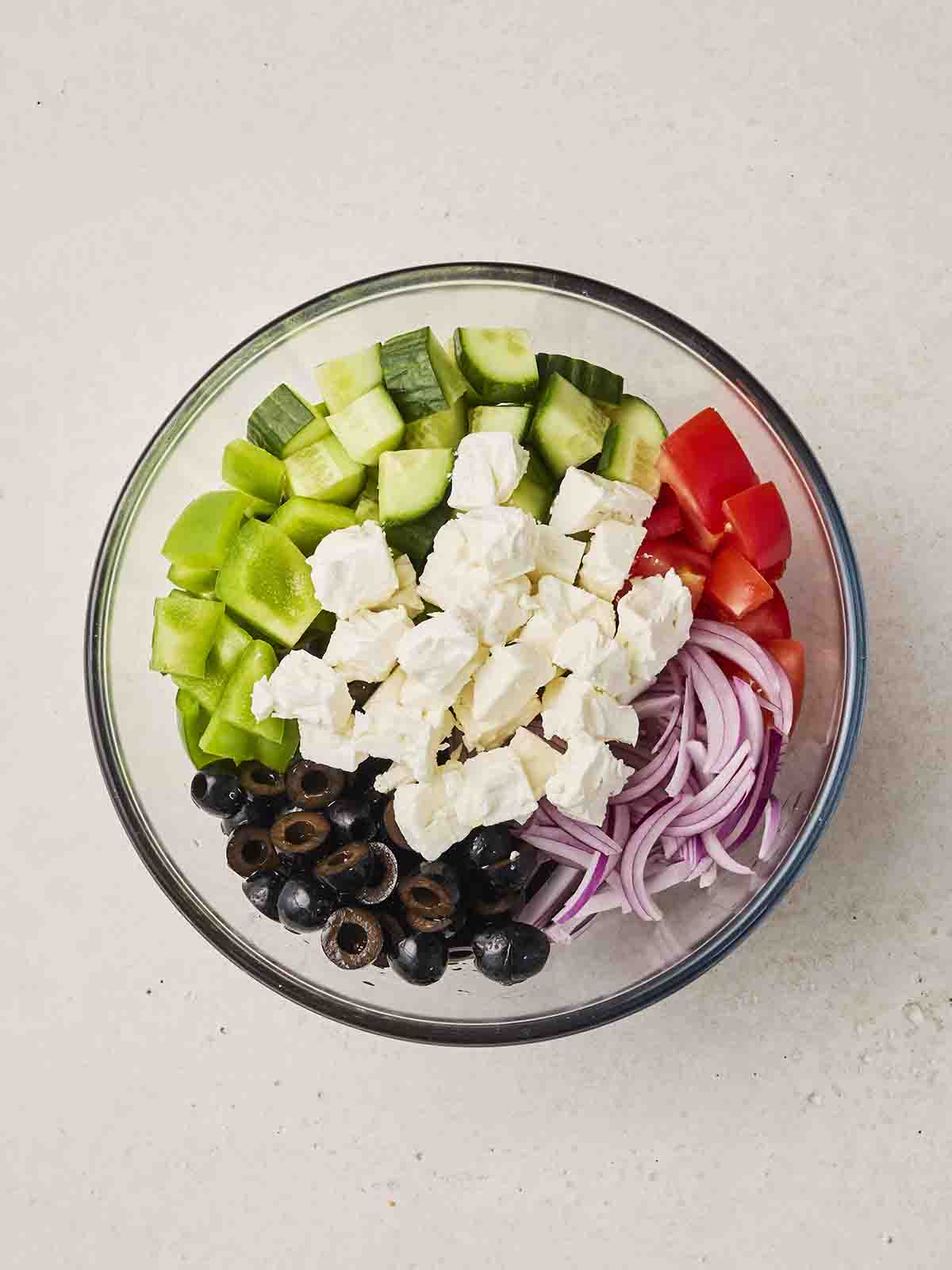 The ingredients for a Greek Salad chopped up in a glass bowl, ready to be mixed.