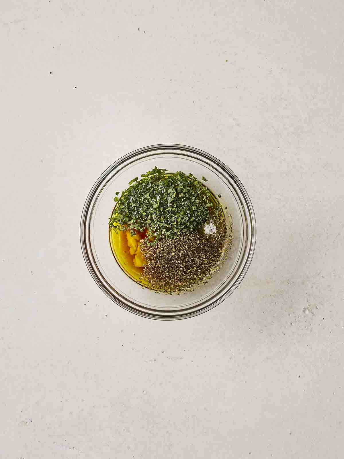 A glass bowl with herbs and oil salad dressing.