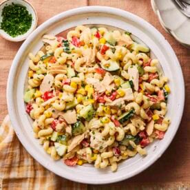 A white plate filled with tuna pasta salad, with dressing to the side.