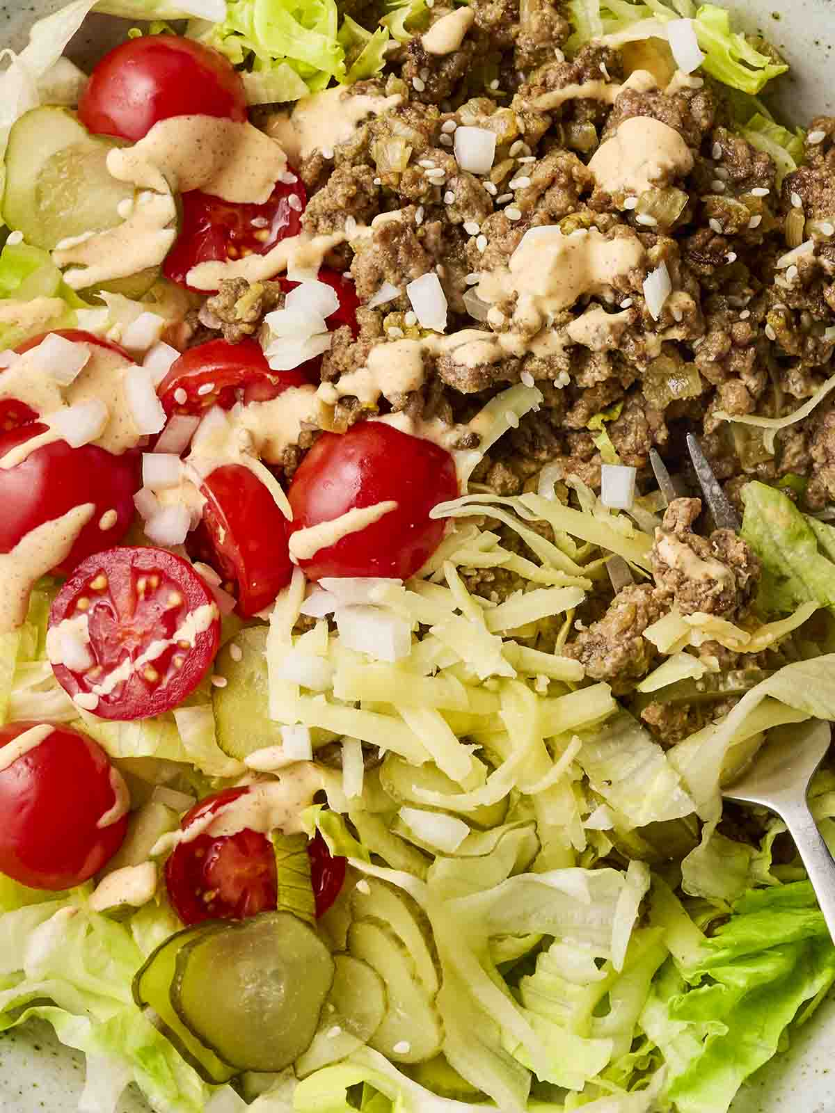 A close up of a salad that looks like a deconstructed Big Mac, with lettuce, tomatoes, gherkins, mince beef and sauce.