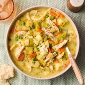 A soup of hearty, creamy soup with chicken and vegetables, with a spoon to serve.