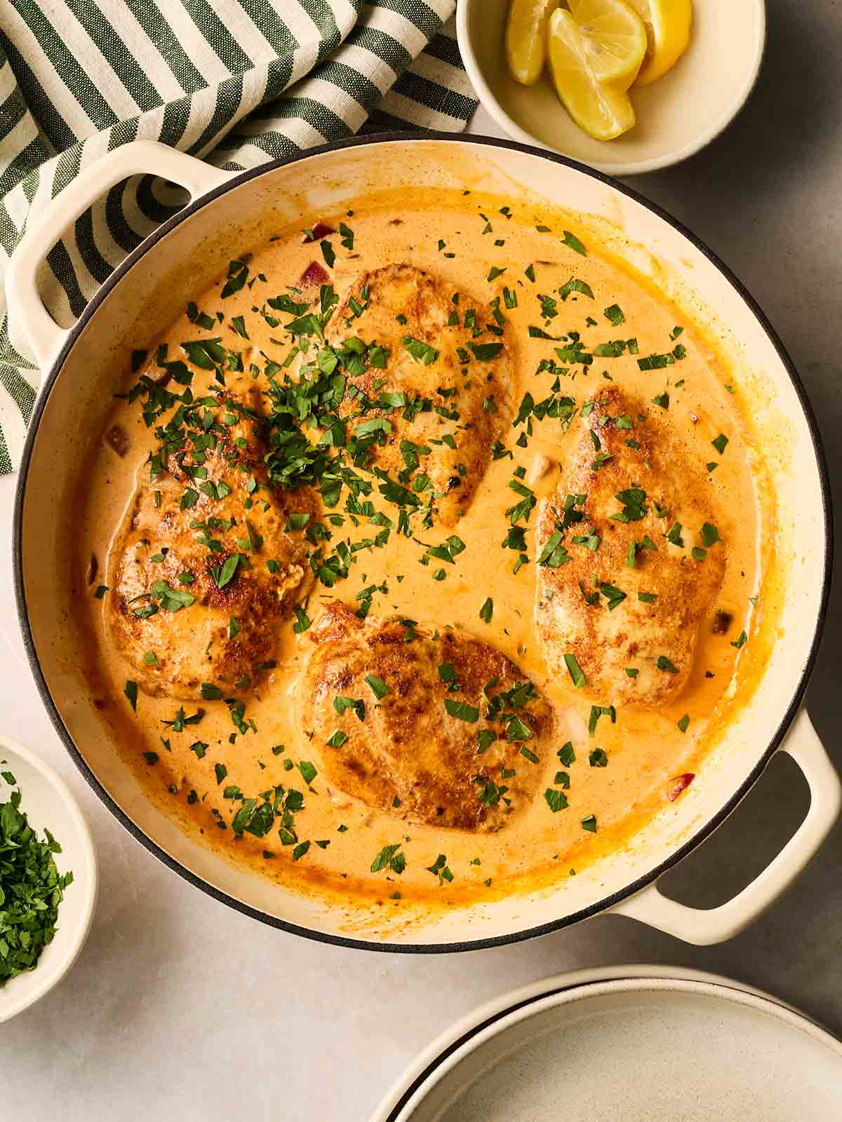 A white pan filled with four chicken breasts in a creamy sauce, with parsley sprinkled over the top.