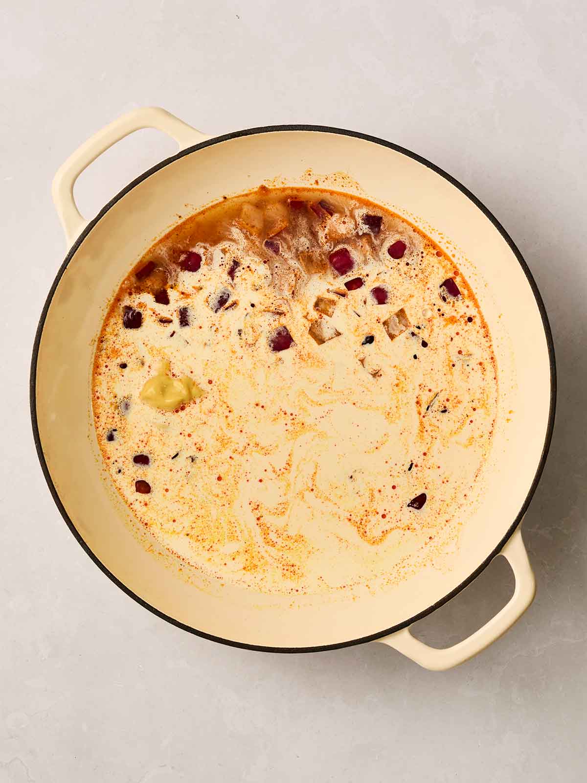 A creamy sauce mixed with red onion and mustard in a pan.