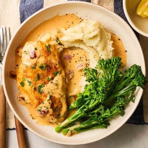 A plate of food, ready to eat, with mash, broccoli and chicken breast in a creamy, paprika sauce.
