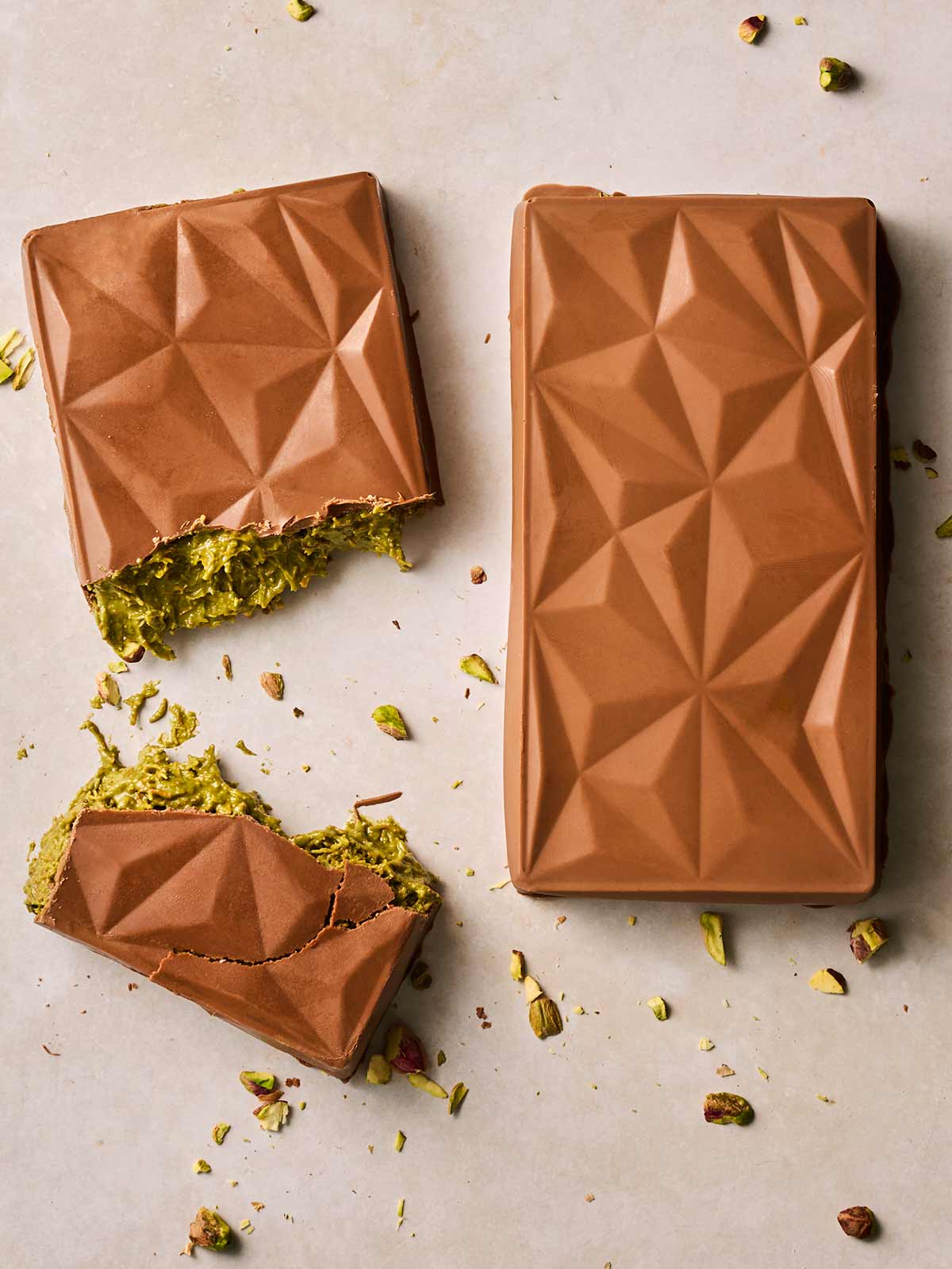 Looking down on two Dubai Chocolate bars. The one on the left has been broken in two to reveal the pistachio pastry inside.