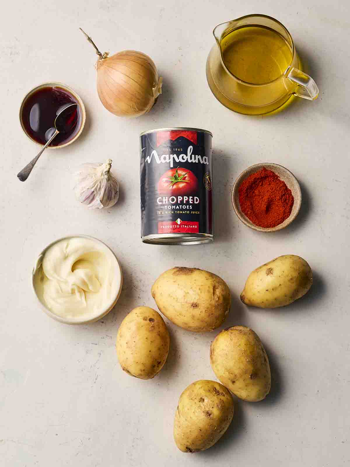 Ingredients laid out on a white surface, including oil, potatoes, mayo, onion, paprika, garlic and sherry vinegar.