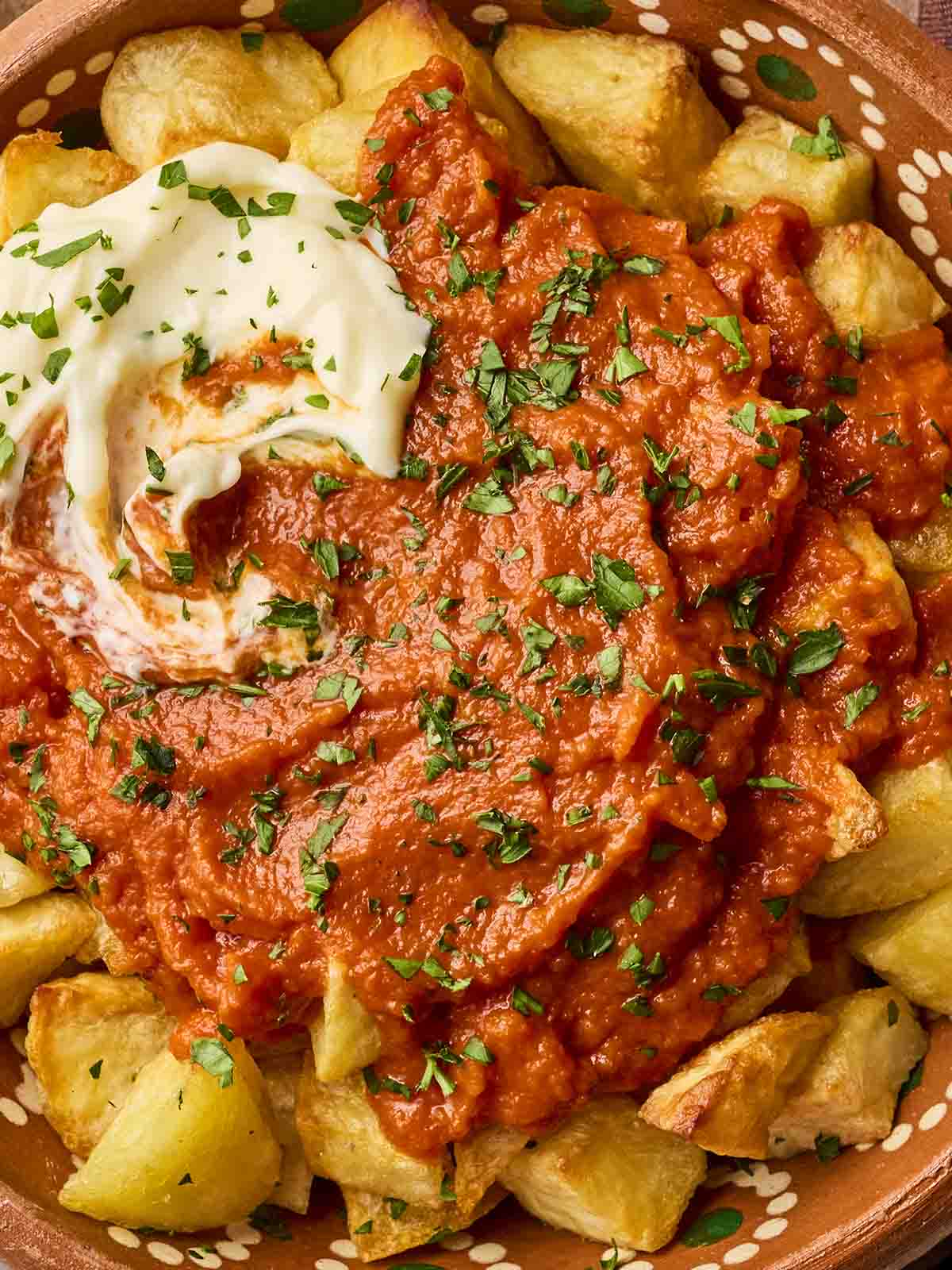 A close up of potatoes covered in tomato sauce with a dollop of mayo for a tapas dish of Patatas Bravas.