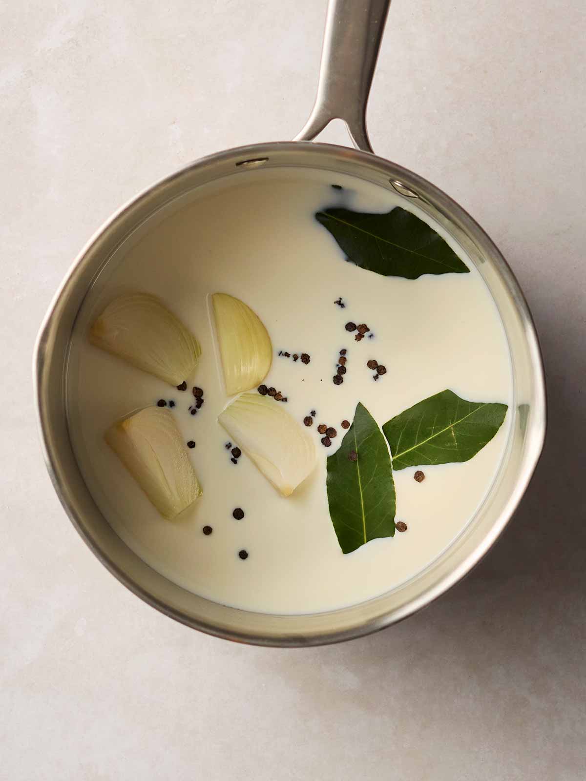 A pan filled with milk, peppercorns, onion and bay leaves.