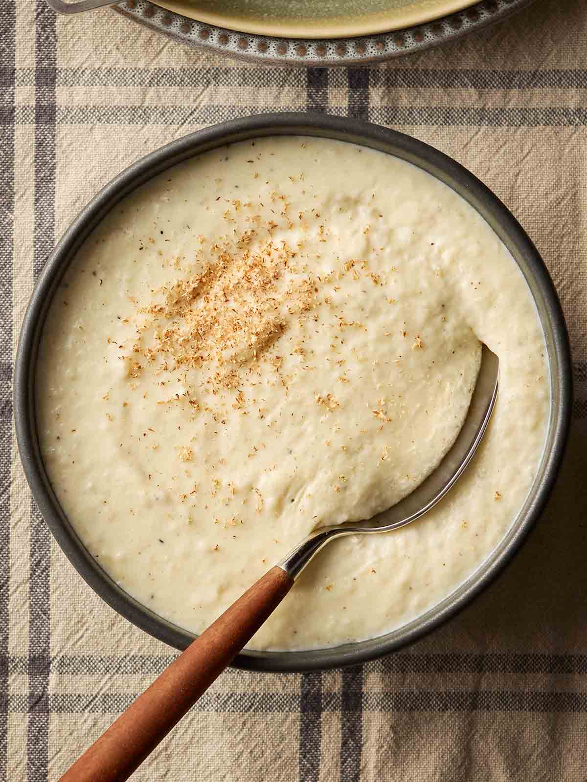 A bowl of condiment Christmas bread sauce on a checked table cloth with a spoon inside it, ready to serve.
