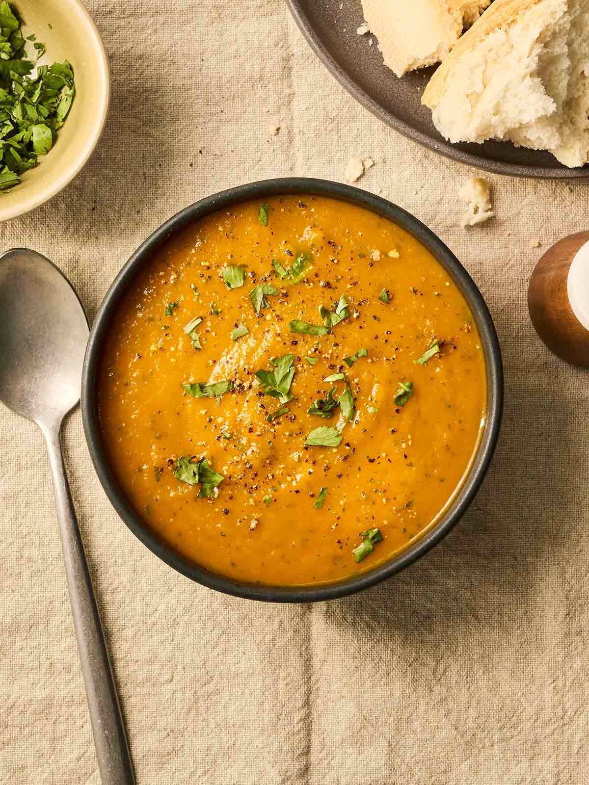 A bowl of orange soup with coriander over the top on a table.