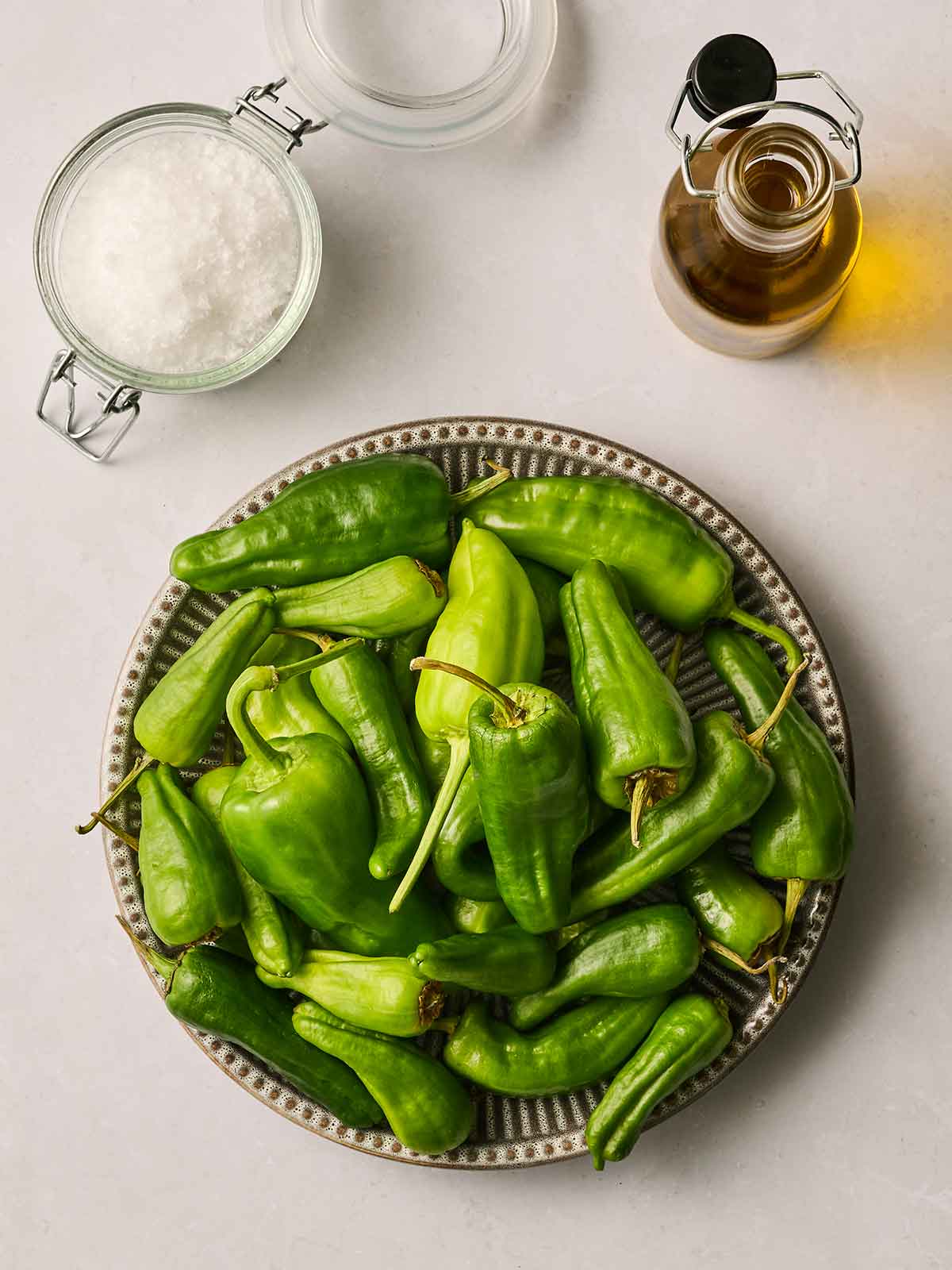 Ingredients for cooking Padron Peppers on a white counter top.