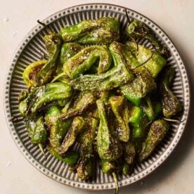 A close up of blisters, salted padron peppers on a stripy plate.