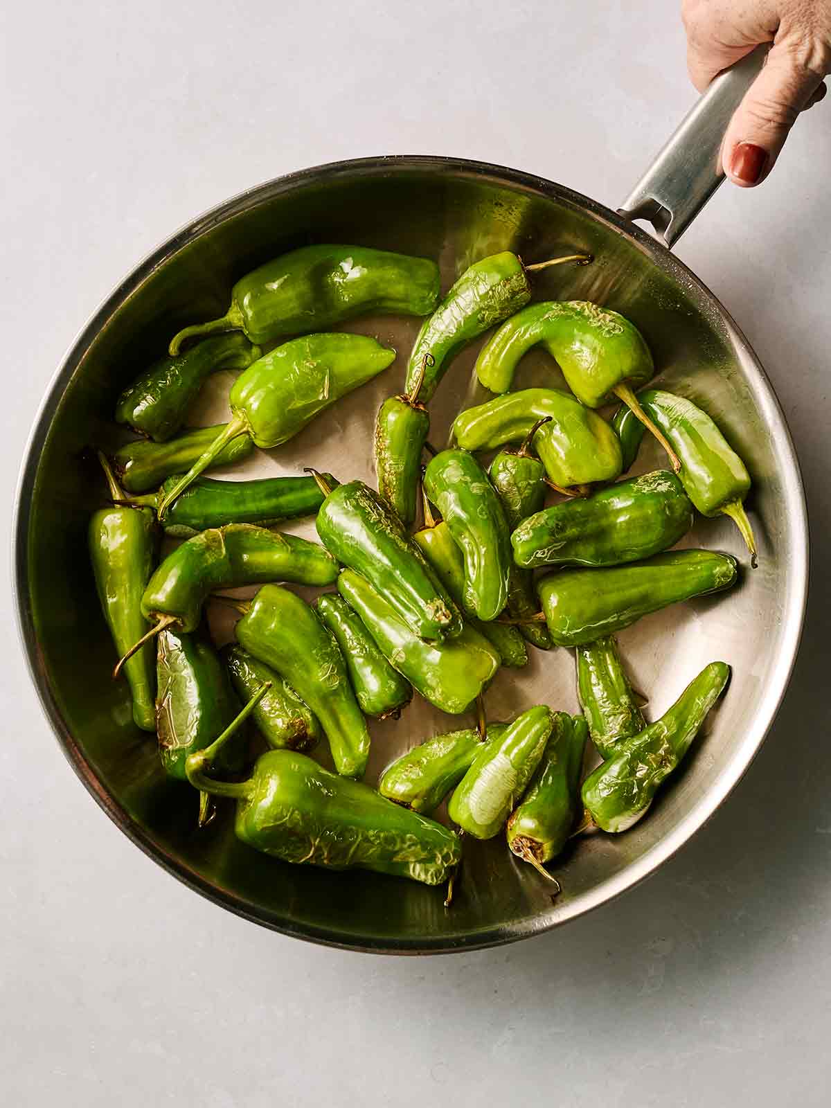 Green padron peppers in a pan with a hand holding the handle.