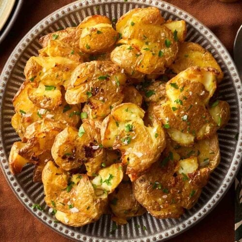 A batch of crushed potatoes with parsley and salt, on a stripy plate, on a brown tablecloth, ready to serve.