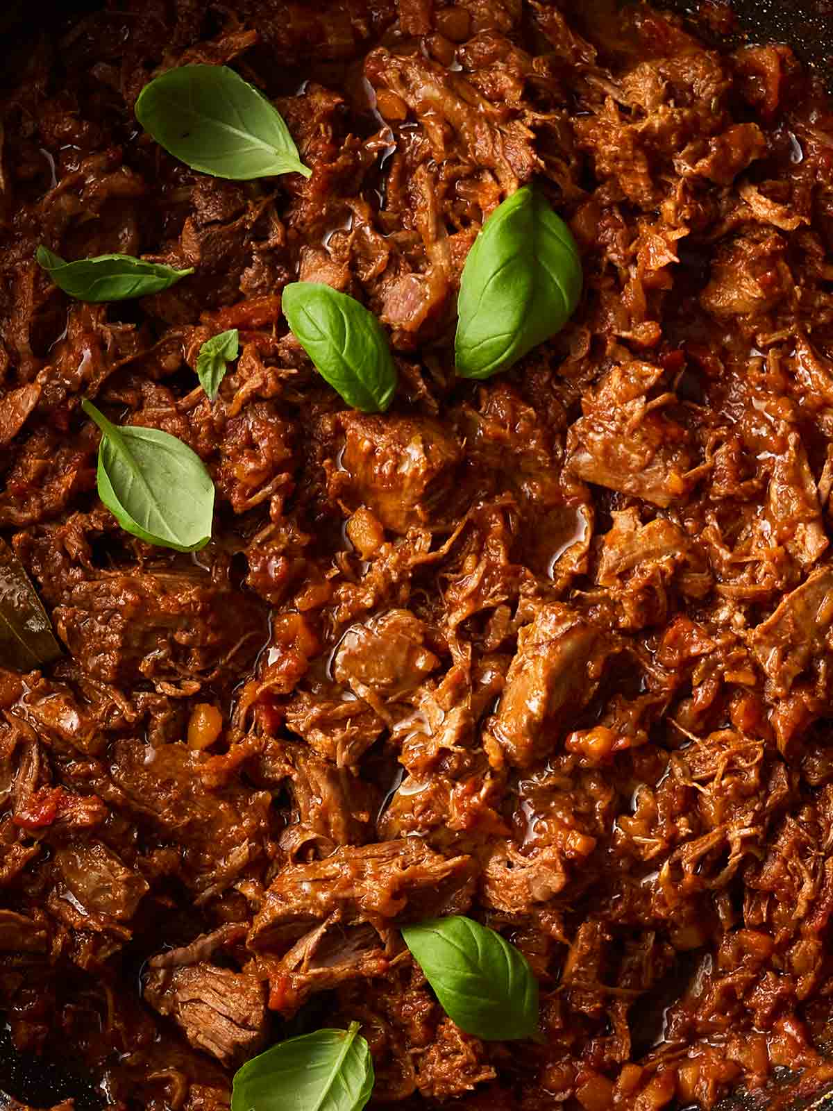 A close up of a batch of beef ragu with basil leaves to garnish on top.