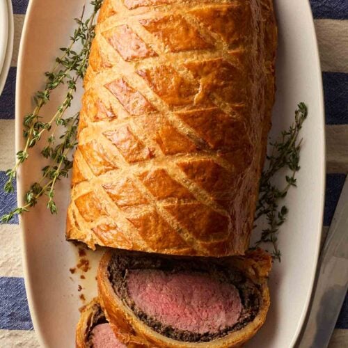 A whole beef wellington on a plate, showing two slices on their side to show the filling.