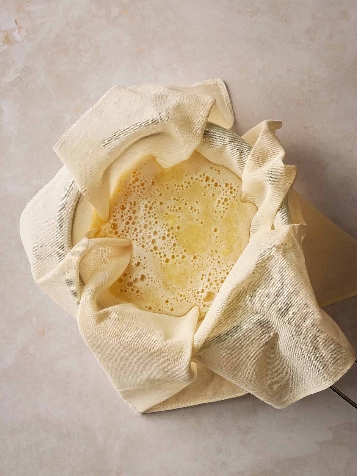 A bowl with a muslin cloth over a sieve with fresh ginger and apple juice going through.