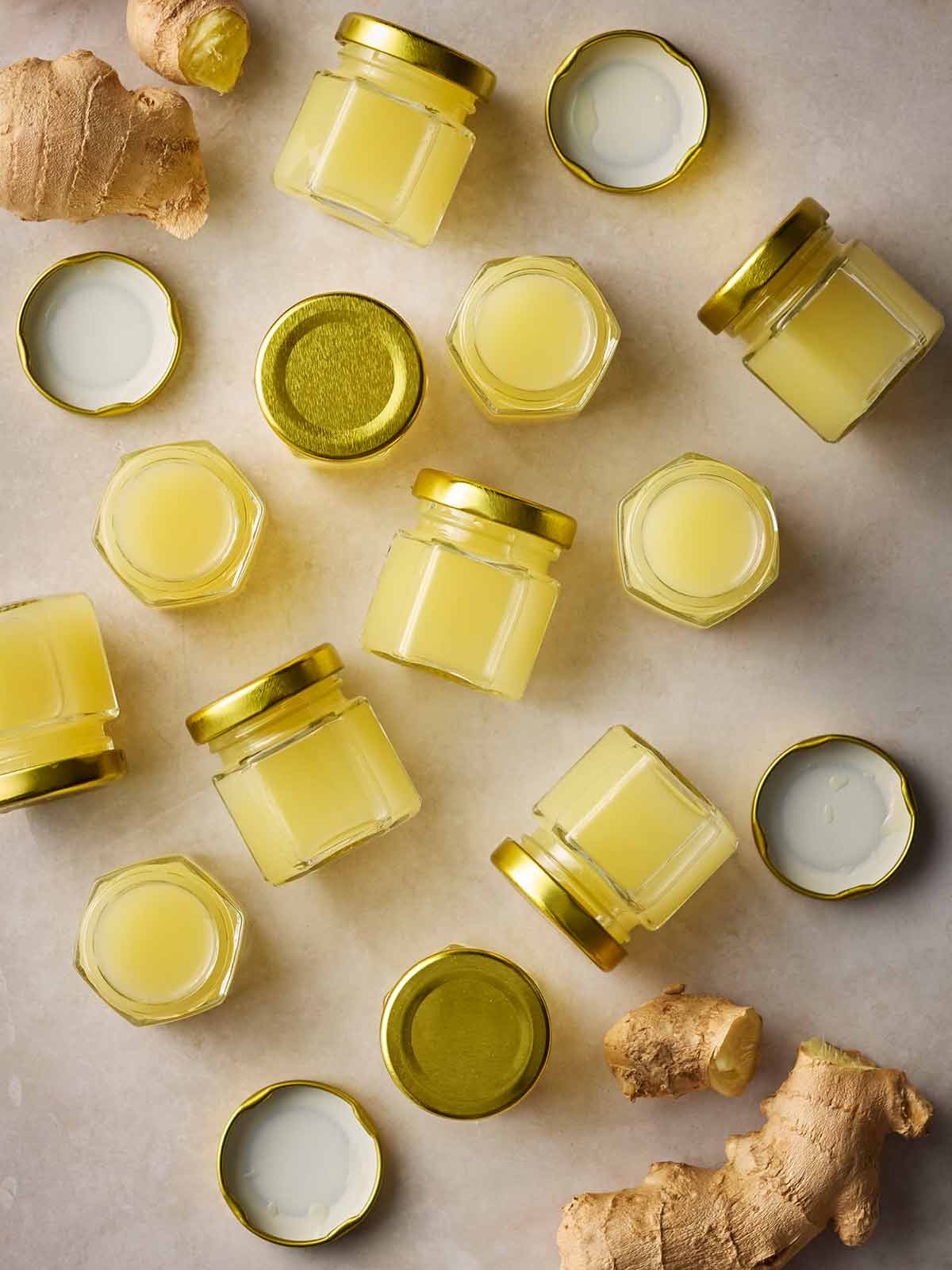 Small pots of ginger shots on a white surface, with fresh ginger around the edges.