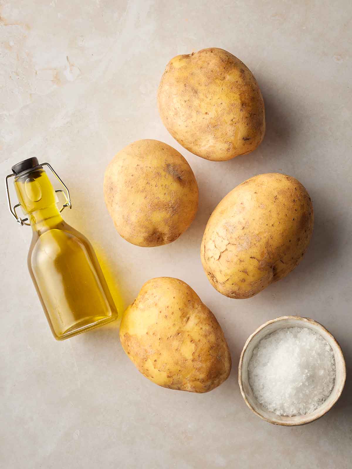 Raw ingredients on a white surface, including potatoes, oil and salt.