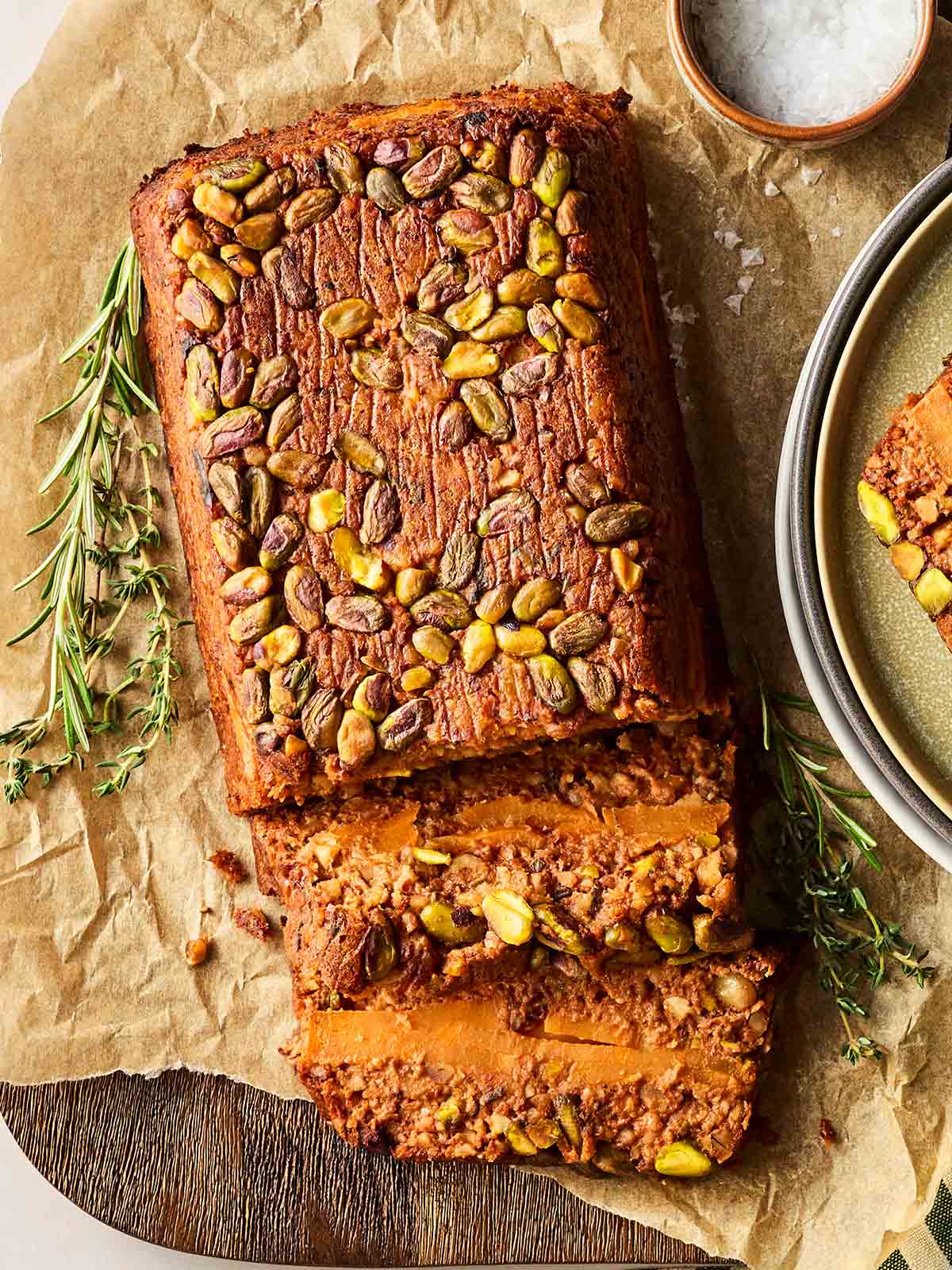 A golden baked nut roast on a sheet of baking paper from above, with rosemary to the side.