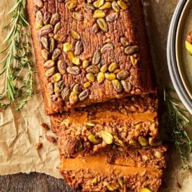 A nut roast on baking paper, with a couple of slices laying down to reveal the inside filling.