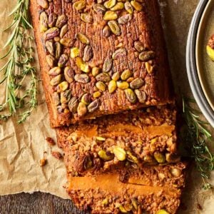 A nut roast on baking paper, with a couple of slices laying down to reveal the inside filling.