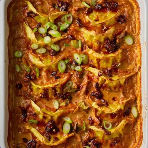 Chinese dumplings in an oven dish with red sauce and vegetables, ready to serve.