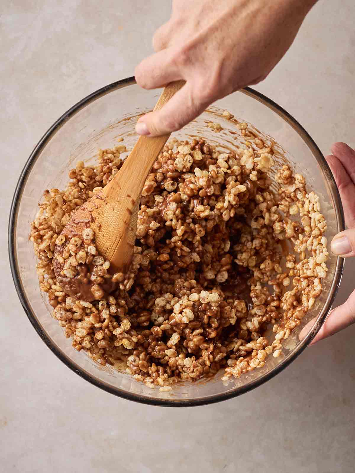 A hand stirring a bowl of rice pop cereal with melted chocolate to make rice crispy cakes.