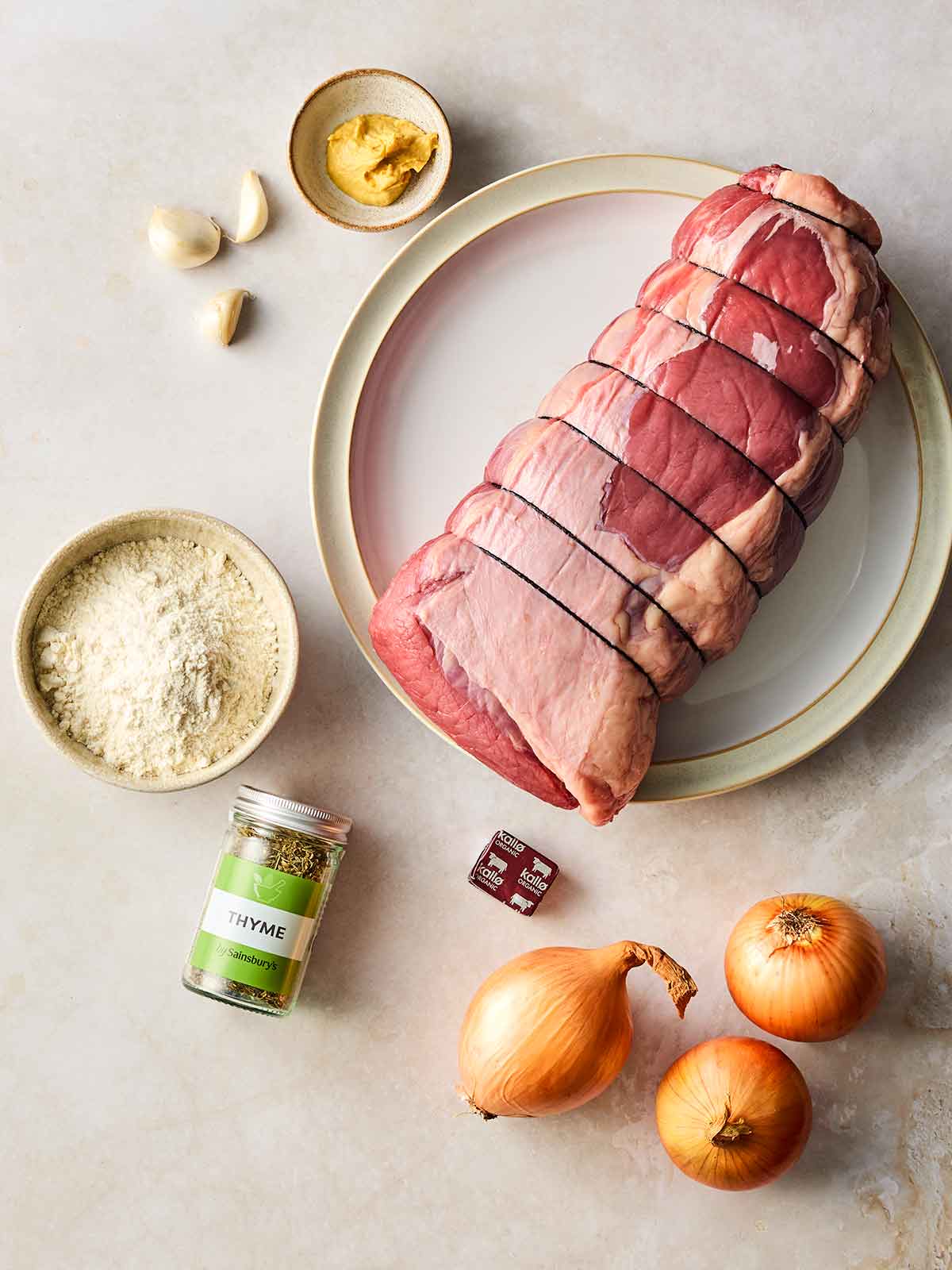 Raw ingredients for making a Roast Beef joint on a white surface.