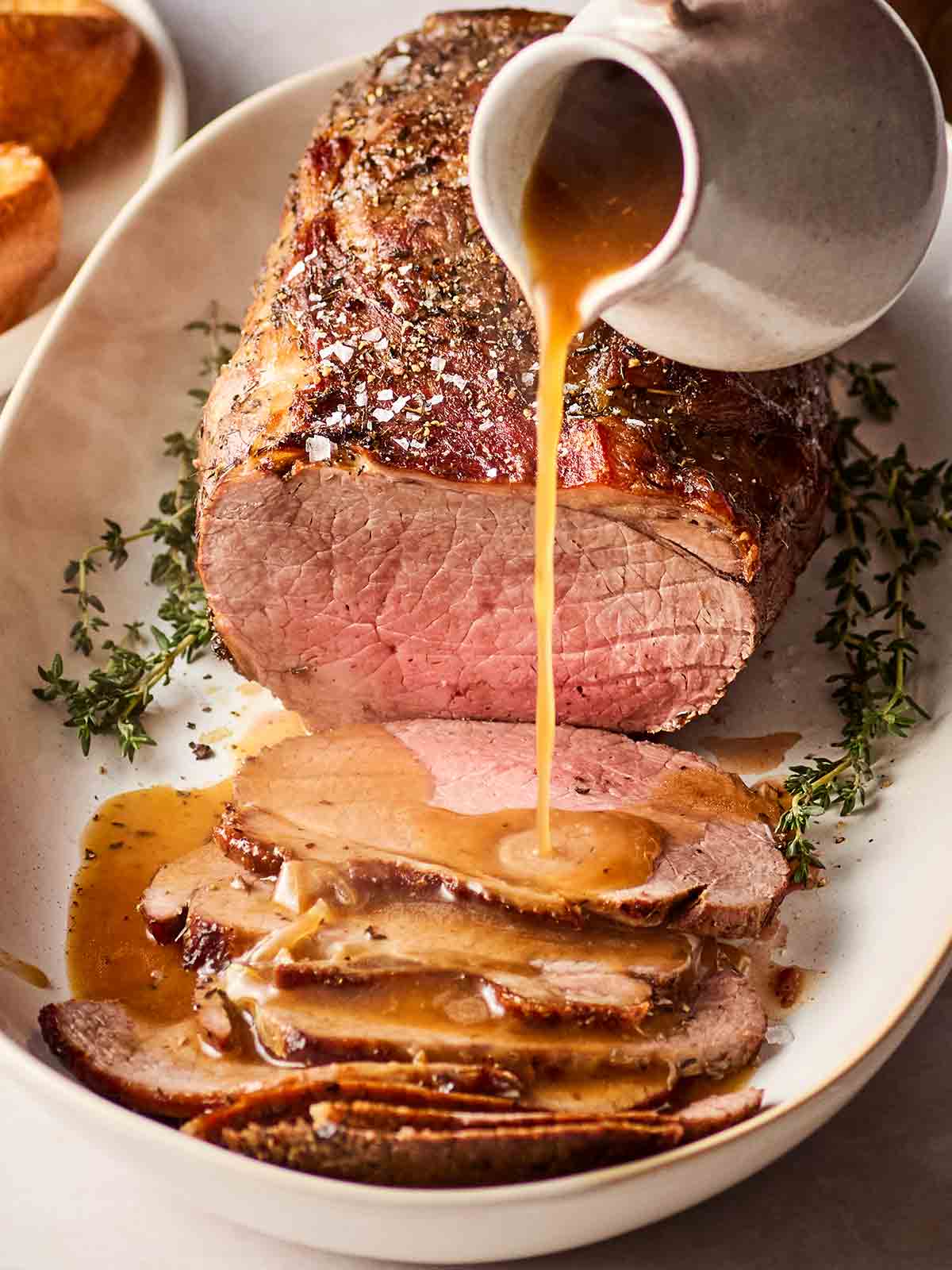 Gravy being poured over a joint of beef slices on a platter.