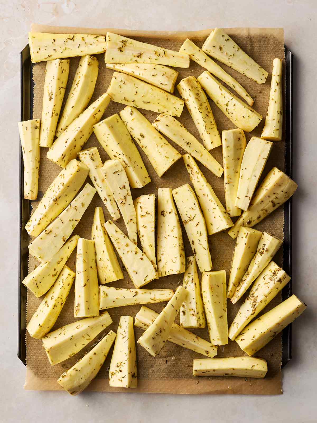 A lined baking tray on a white surface, with chopped and coated parsnips ready to roast.