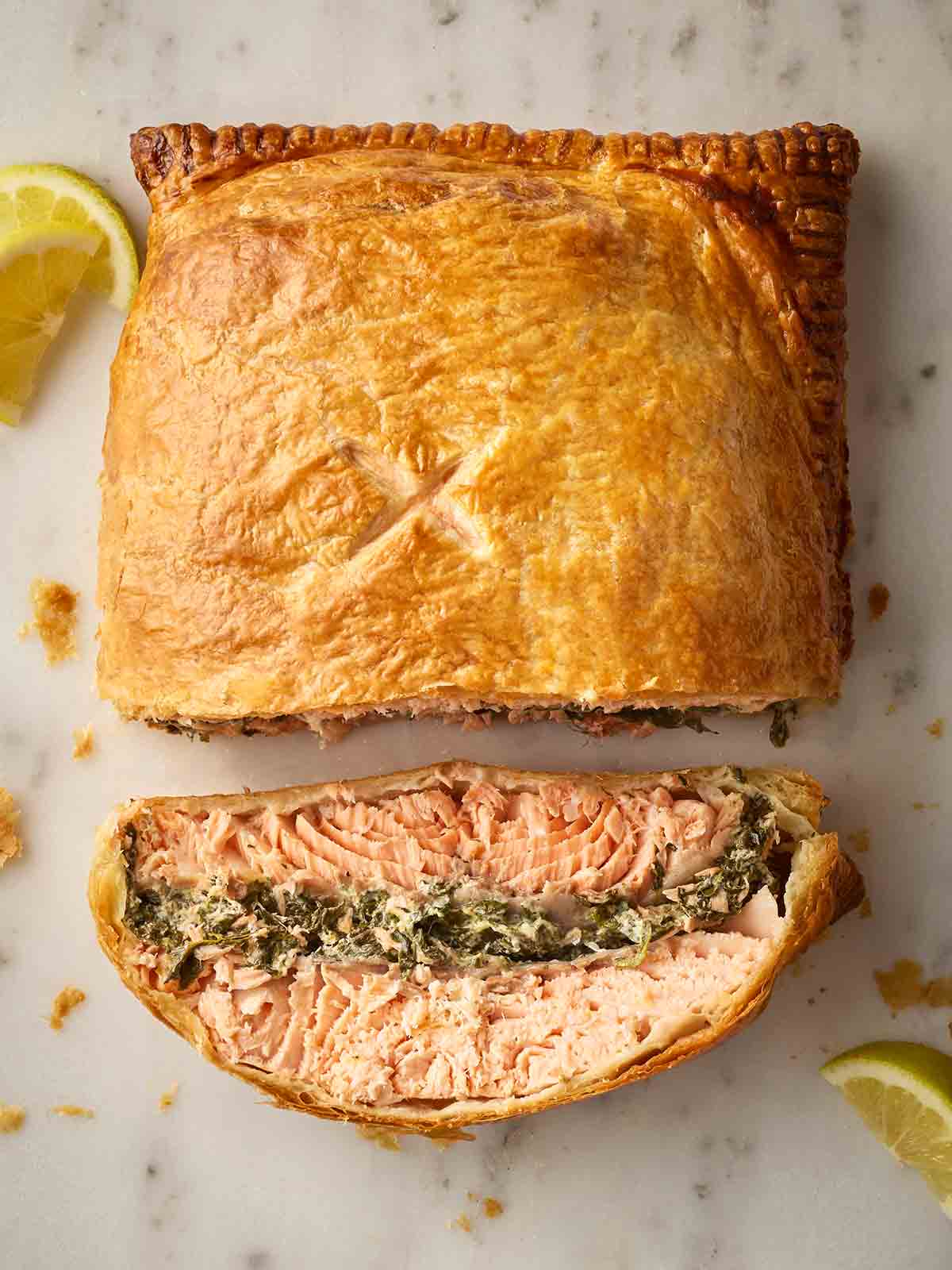 A Salmon en Croute laid on a white counter, with a slice laying down to reveal the filling of salmon and cheese spinach in a pastry crust.