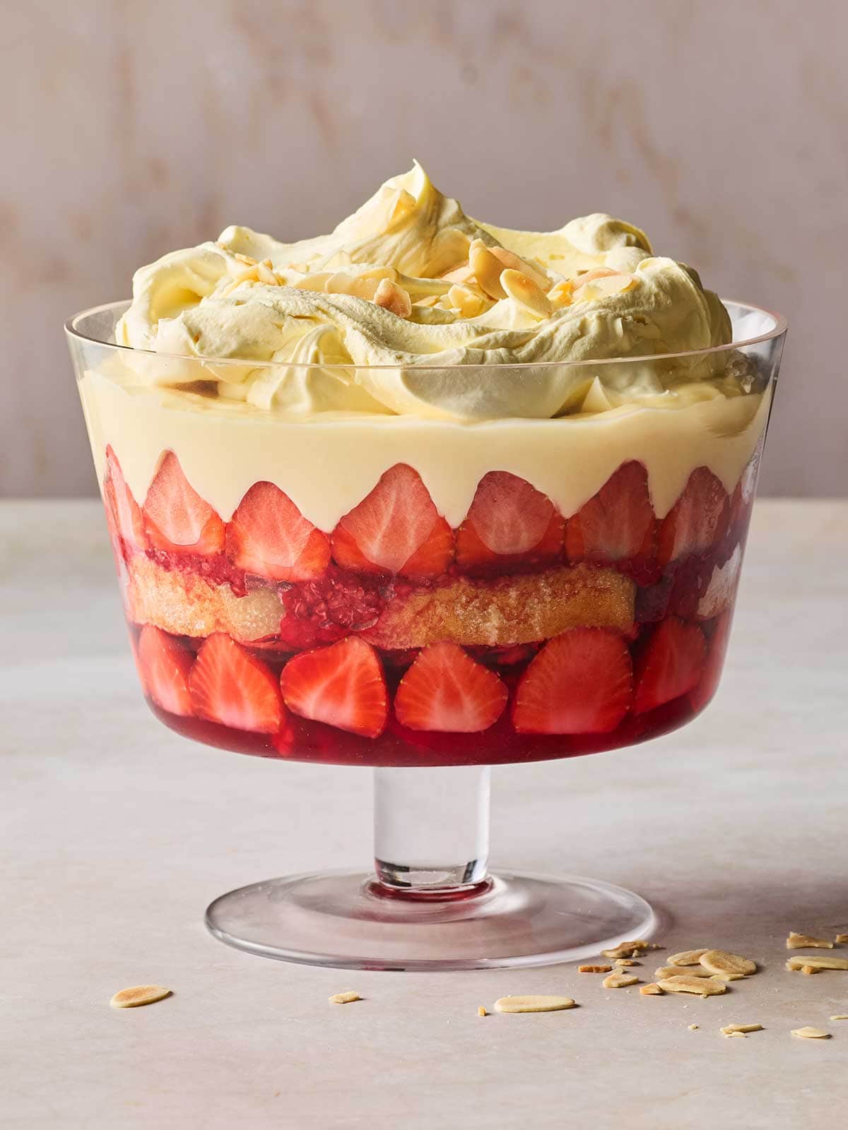A side view of a classic Trifle in a glass dish on a white surface.