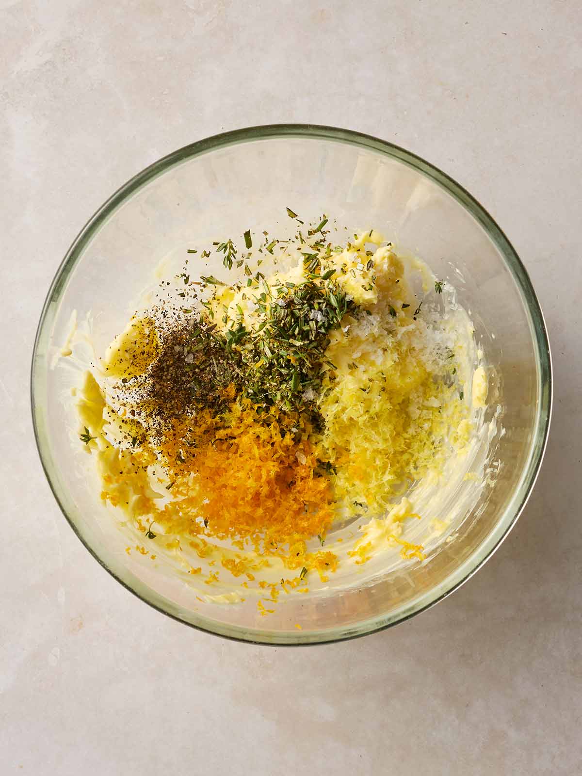 A glass bowl filled with butter, herbs and orange and lemon zest.