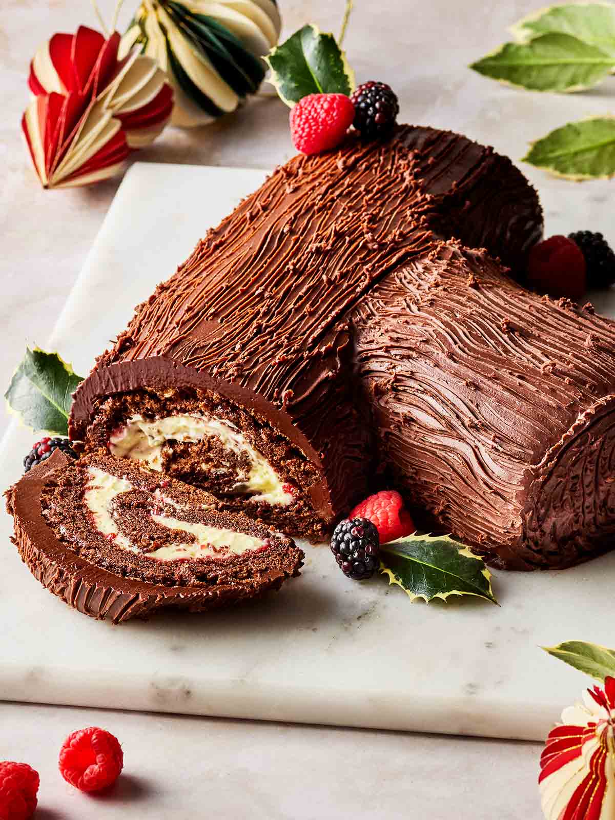 A homemade Christmas Yule Log laid out on a surface, with one slice cut to show in the filling.