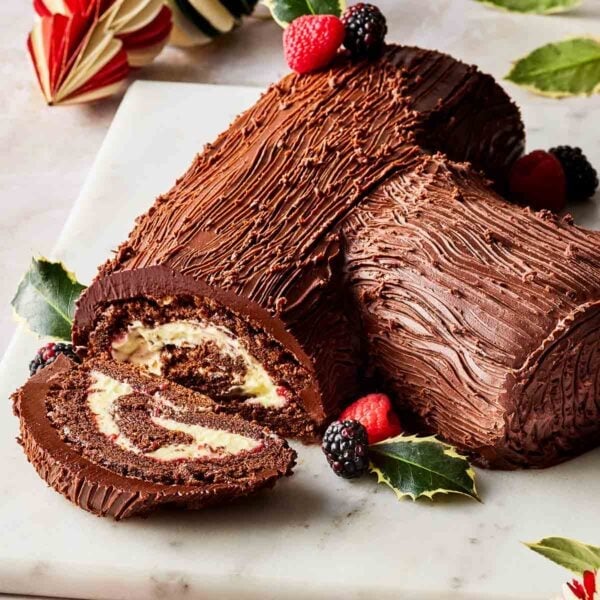 A Christmas yule log on a board, with a slice out to show the insides, and decorated with holly and berries.