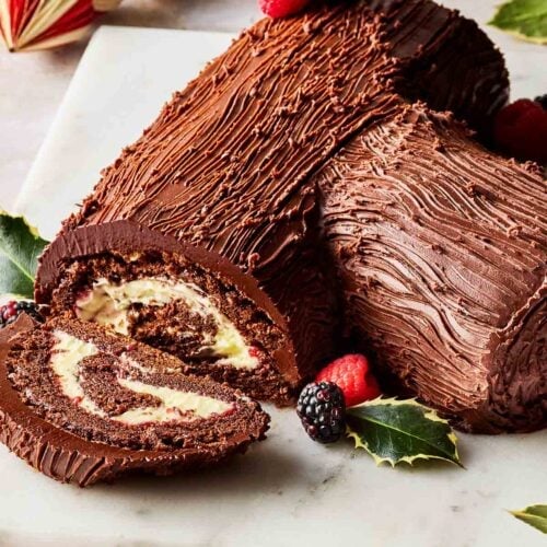 A traditional chocolate log decorated with Christmas berries and holly.