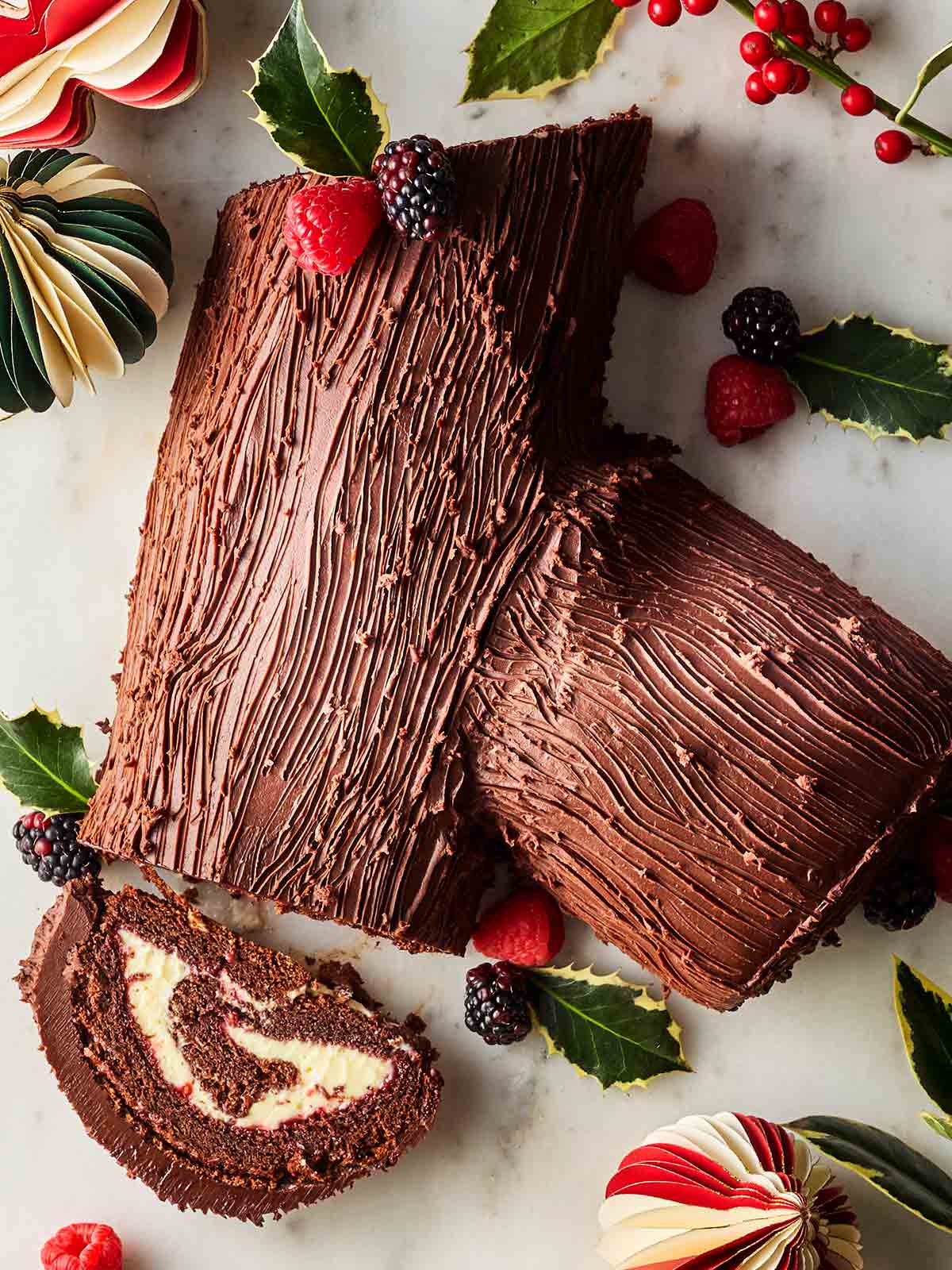 A bird's eye view of a Christmas Yule Log, with a slice on its side to show the rolled creamy cake filling.