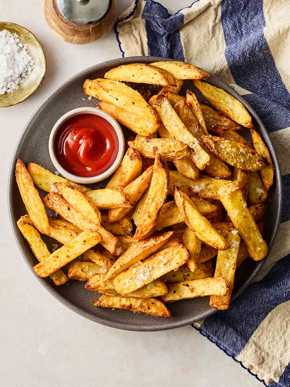 A batch of homemade air fryer chips on a plate with a small bowl of ketchup.