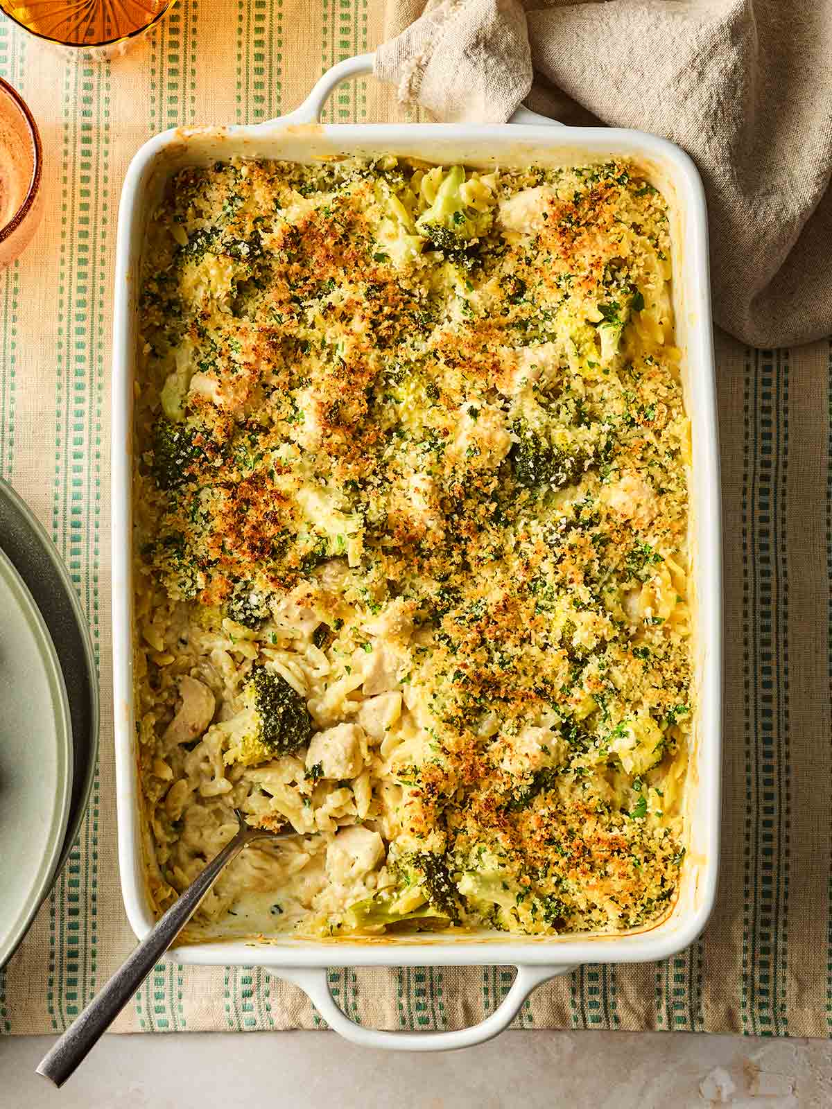 An oven dish on a table with a one pan meal, ready to serve, with chicken, broccoli and orzo in a garlic, creamy sauce.