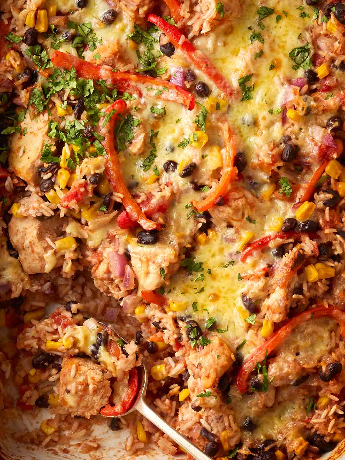 A close up of a one pan dinner, with chicken, rice, beans and peppers with cheese for a Burrito-style recipe.