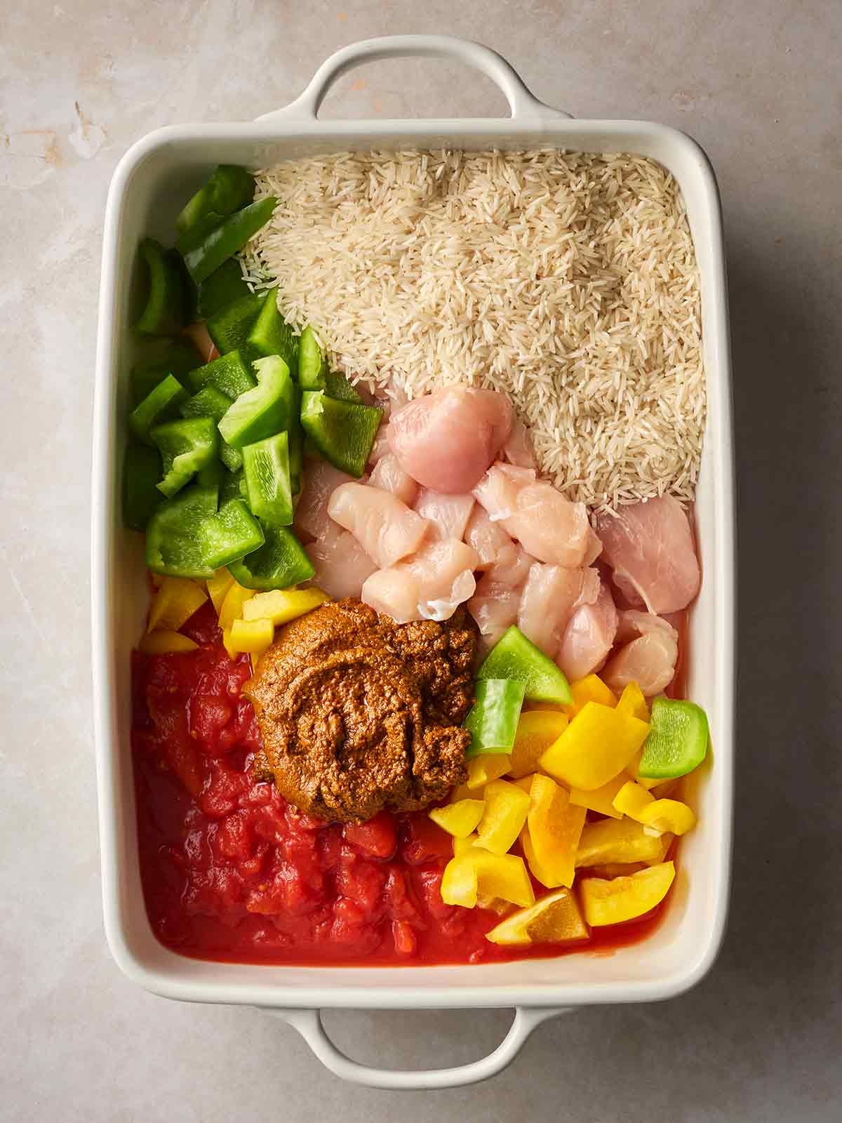 An oven dish filled with raw chicken and rice, curry paste, peppers and tinned tomatoes.